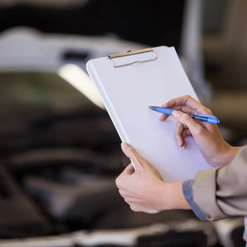 Mãos segurando uma prancheta de papel em branco diante do motor de um carro